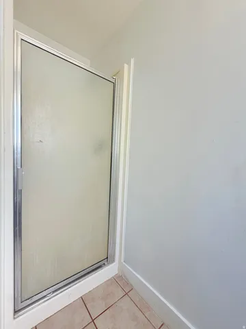 Enclosed shower stall with a frosted glass door and a metal frame, set on light-toned tile flooring