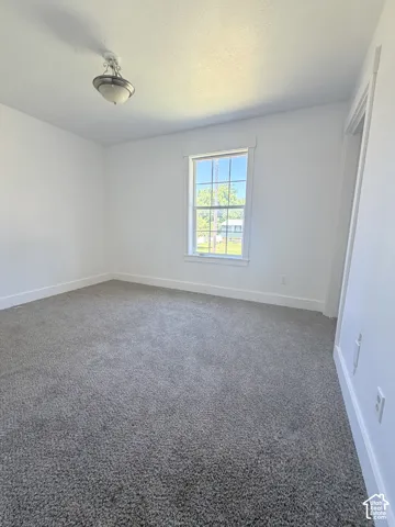 Bright room featuring a window with white trim, gray carpet flooring, white walls, and a ceiling-mounted light fixture