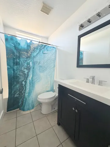 Bathroom featuring a black vanity with a white countertop and integrated sink, chrome faucet, wall-mounted mirror, and tile flooring