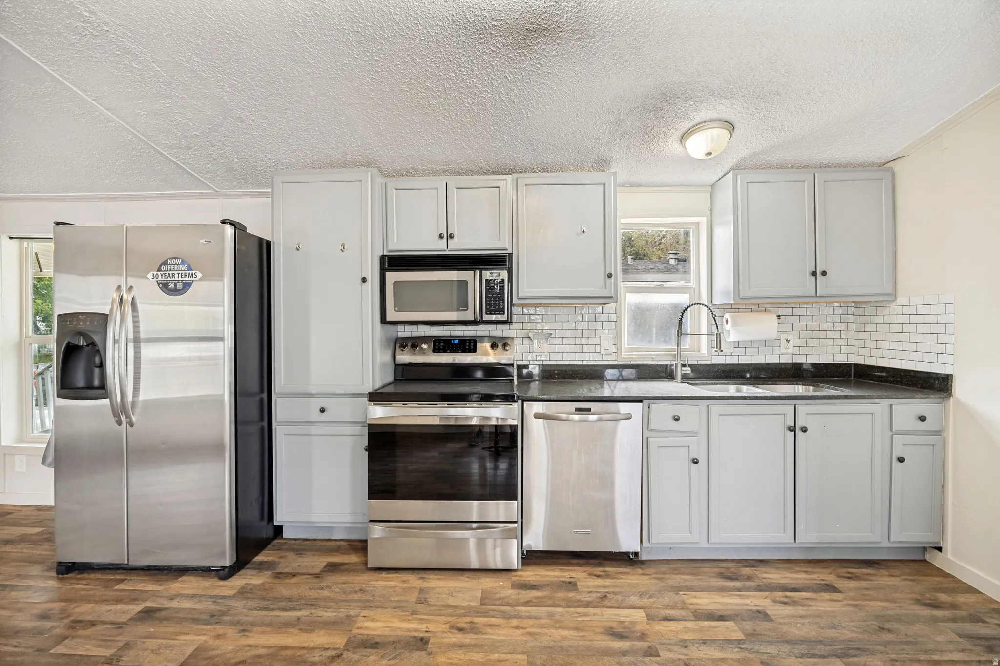 Kitchen featuring light gray cabinetry, dark countertops, white subway tile backsplash, and wood-finish flooring