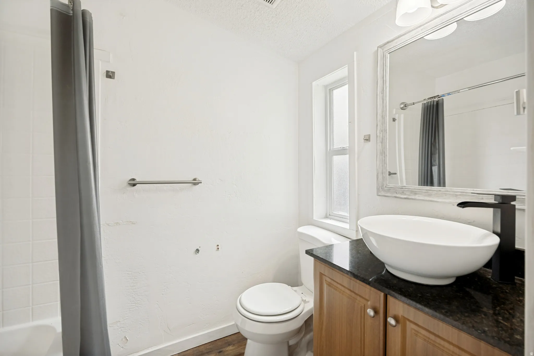 Bathroom featuring a vessel sink, dark countertop, wood-finish vanity, and a window for natural light