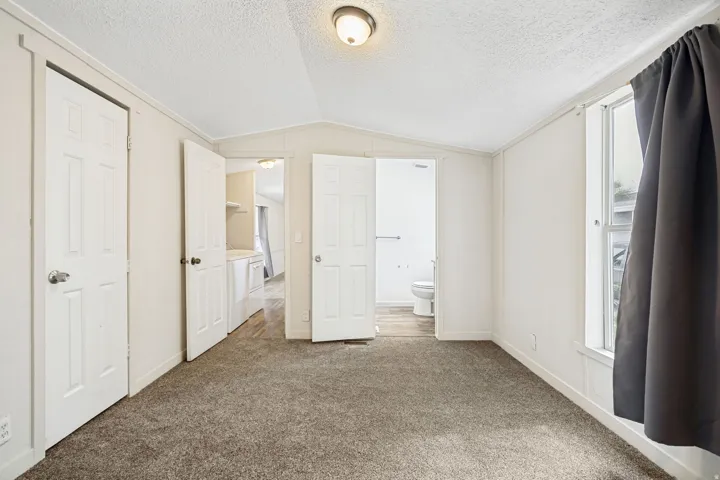 Carpeted room featuring white walls, a flush-mount ceiling light, and a window with dark drapes