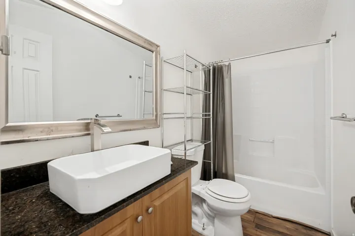 Modern bathroom featuring a rectangular vessel sink, dark granite-finish countertop, and wood-finish flooring