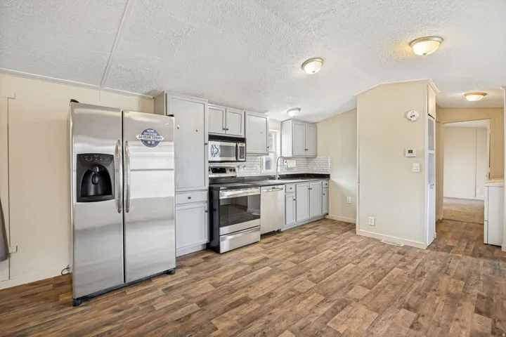 Kitchen featuring wood-finish flooring, stainless steel appliances, light gray cabinetry, and a subway tile backsplash