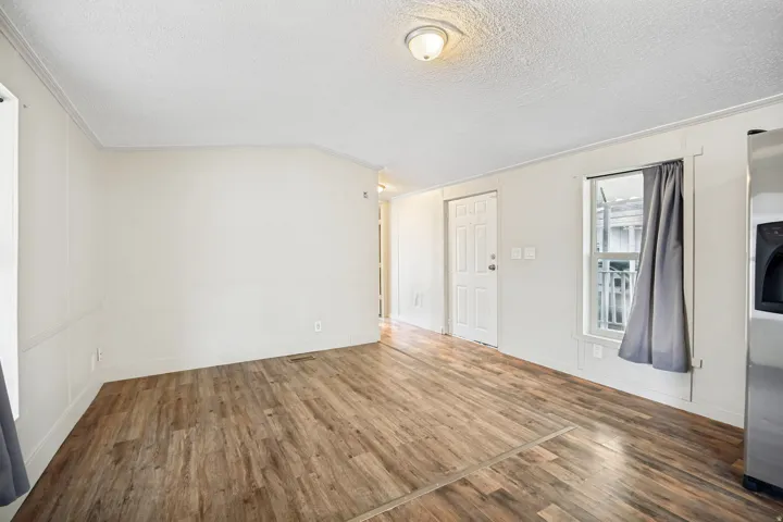 Open living space featuring wood-finish flooring, white walls with wainscoting, an overhead flush-mount light fixture, and a white paneled door