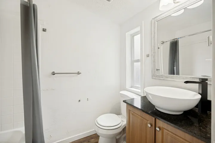 Bathroom featuring a vessel sink, dark countertop, wood-finish vanity, and a window for natural light