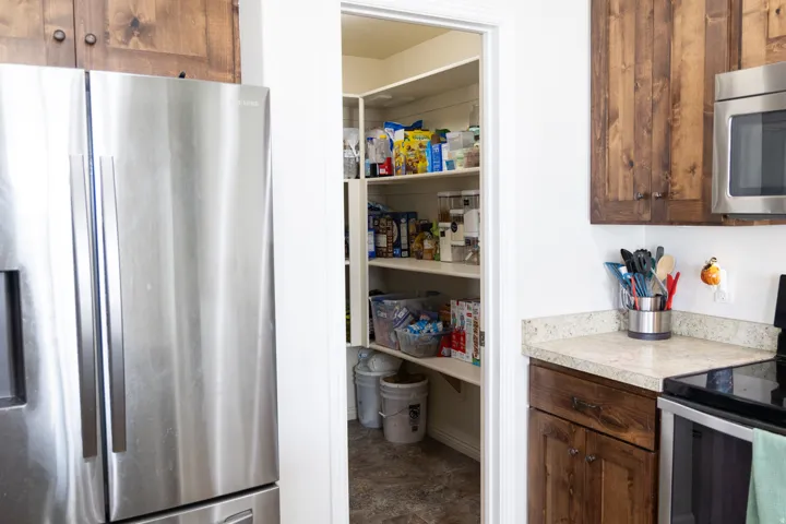 Walk-in pantry with extensive shelving, stainless steel appliances, wood-finish cabinetry, and light-toned countertops