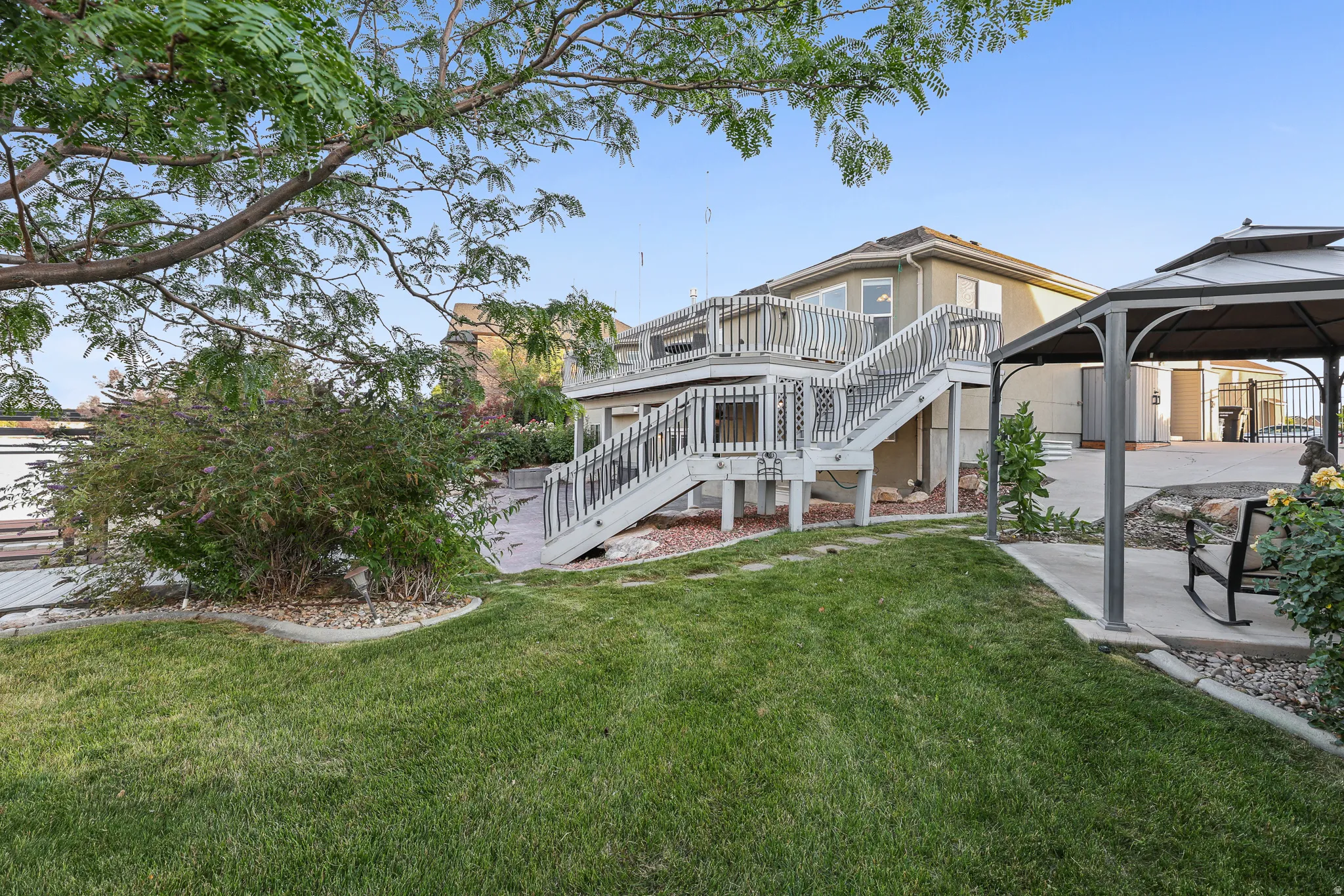 Expansive backyard featuring a multi-level deck with white railings, a concrete patio, and a covered gazebo