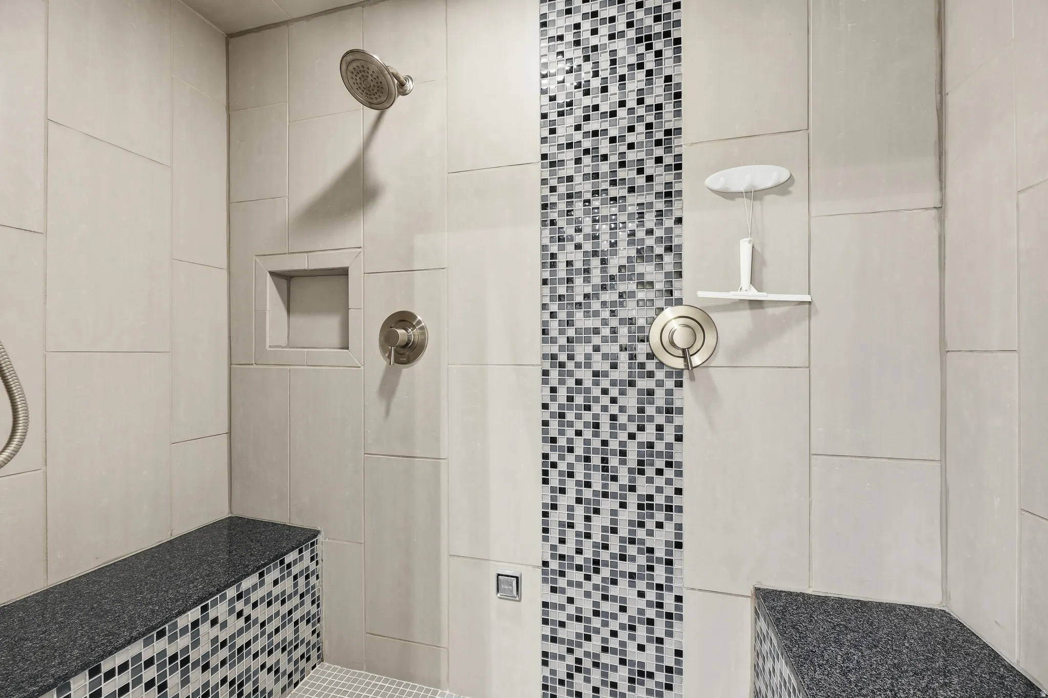 Tiled shower featuring a rain showerhead, built-in niche, dual shower controls, and two integrated benches with granite tops