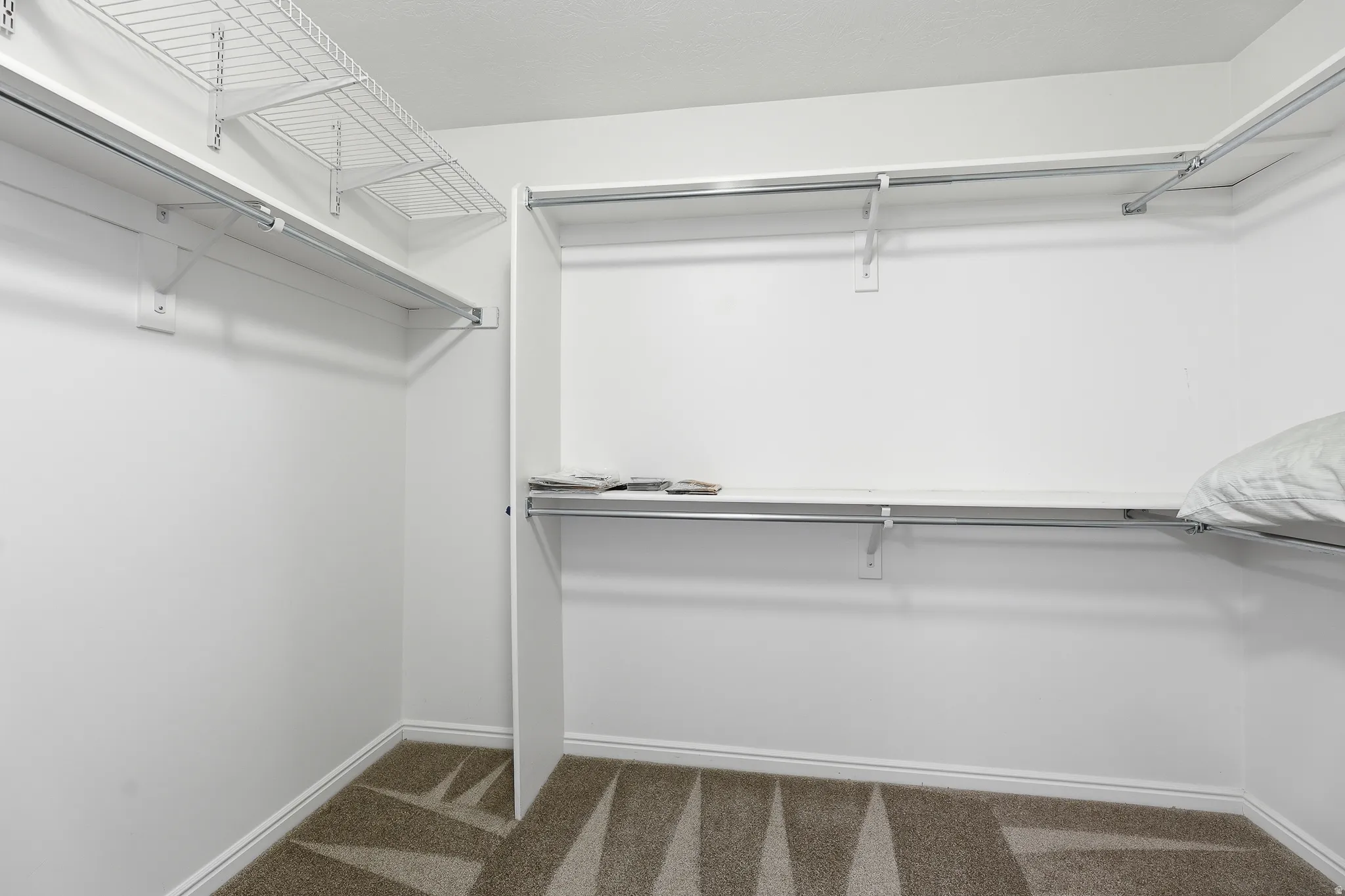 Primary Walk-in closet featuring white wire shelving, hanging rods, and patterned carpeting