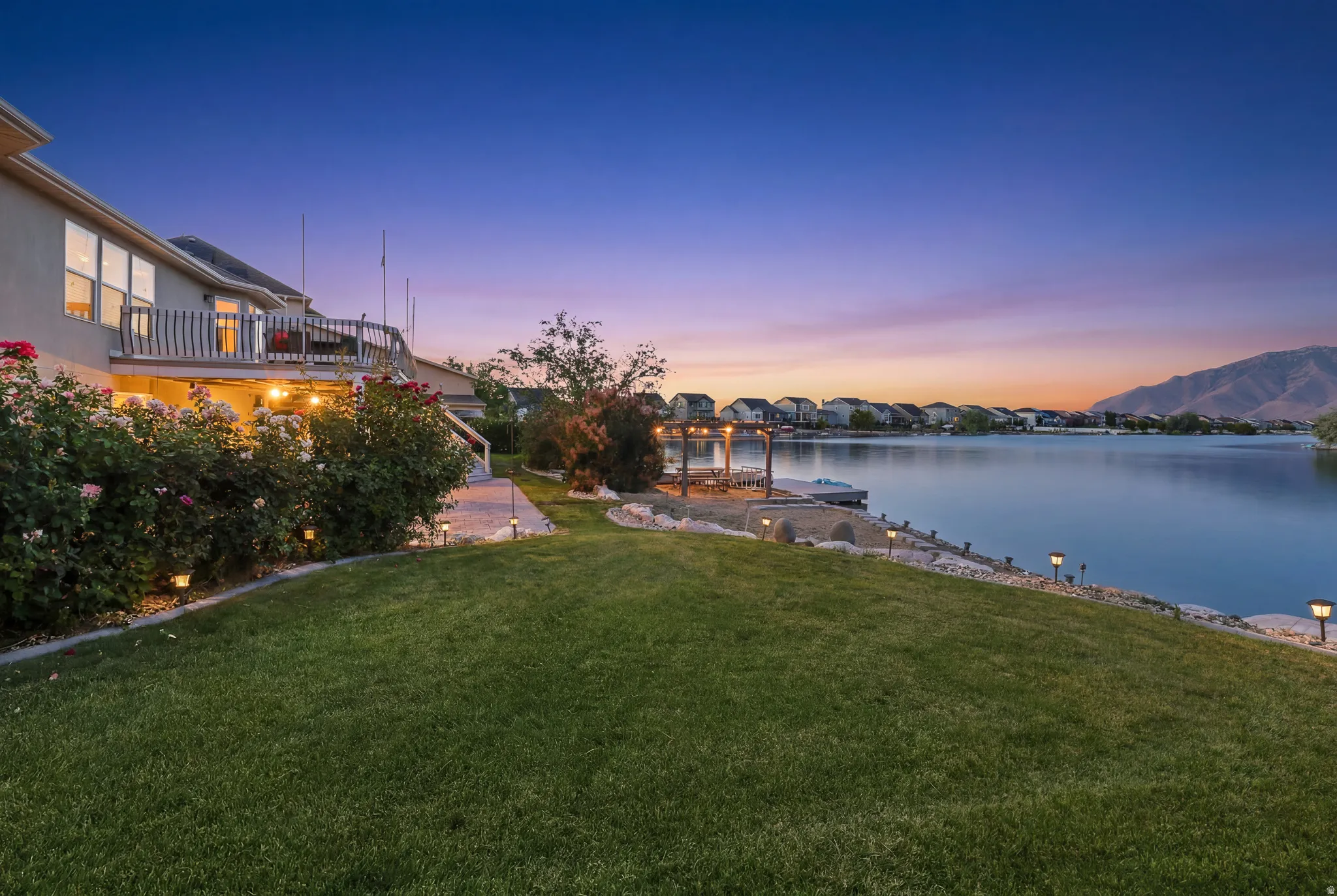 Expansive waterfront property featuring a manicured lawn, established landscaping, and a multi-level deck