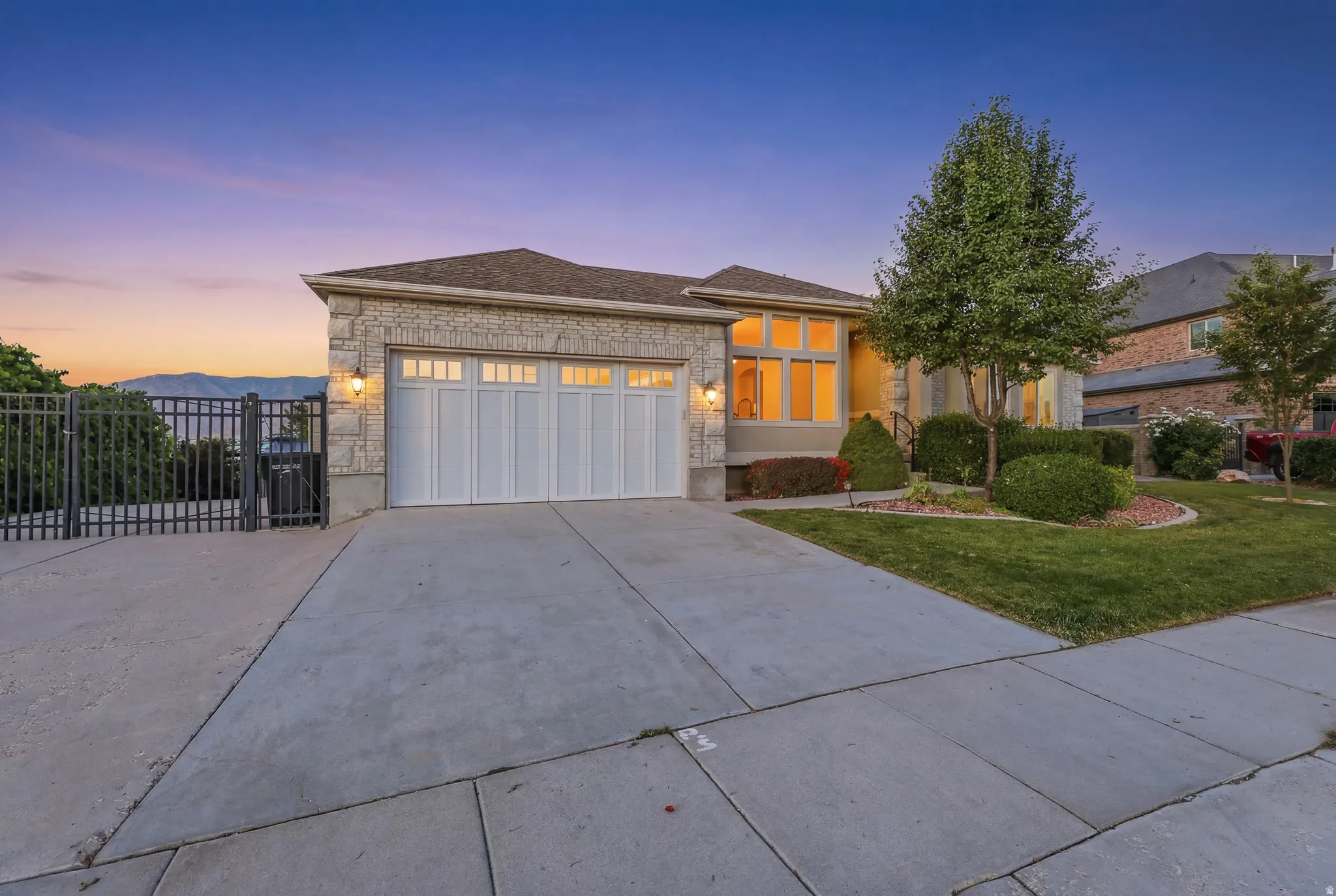 RV Parking, Stone veneer facade with a two-car garage, showcasing a concrete driveway and sidewalk, front lawn with mature trees and shrubs, and a side gate