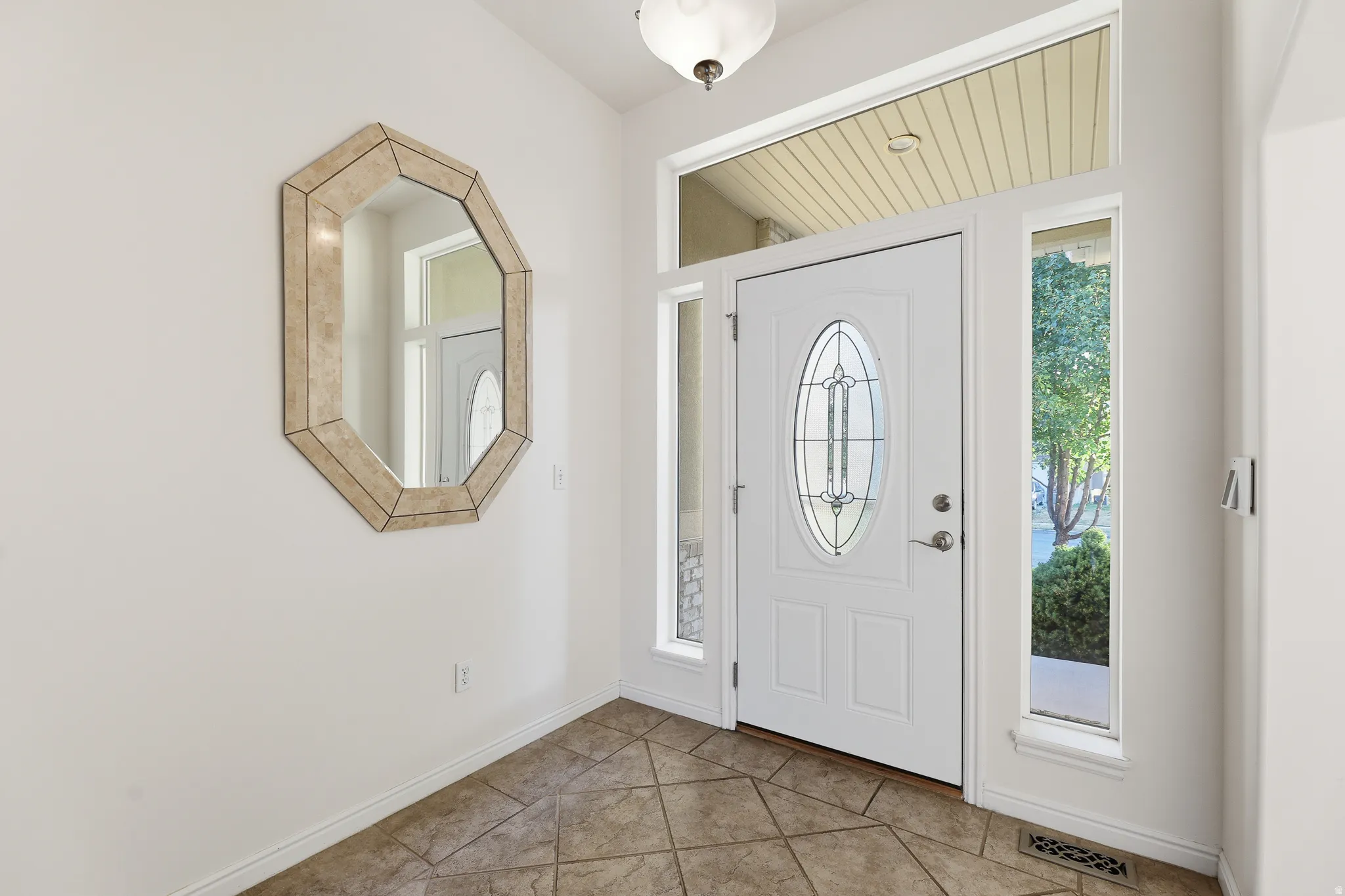 Entryway featuring a white door with an oval leaded glass insert, flanked by sidelight windows and topped with a transom window