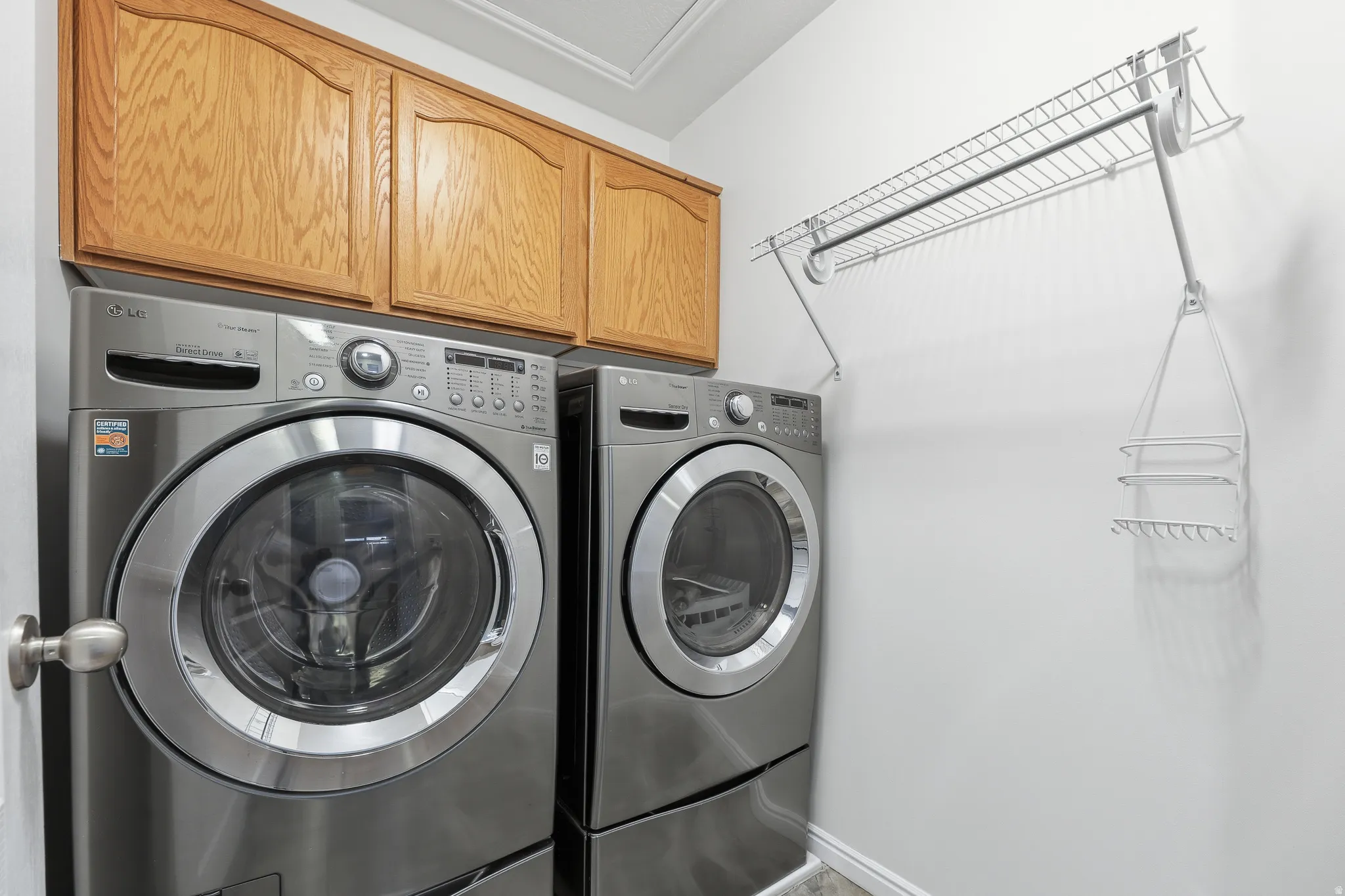 Laundry area with wood-finish cabinetry, front-loading appliances, and a wall-mounted wire drying rack with integrated shelving