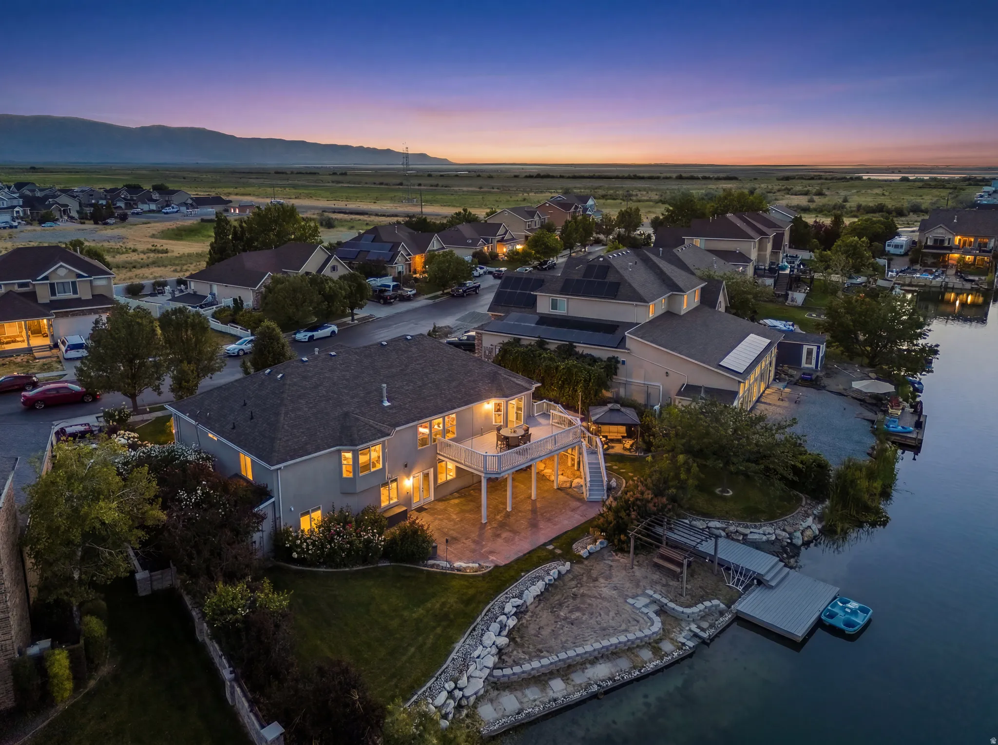 Waterfront residence featuring an expansive deck, lower patio, private dock, and mature landscaping