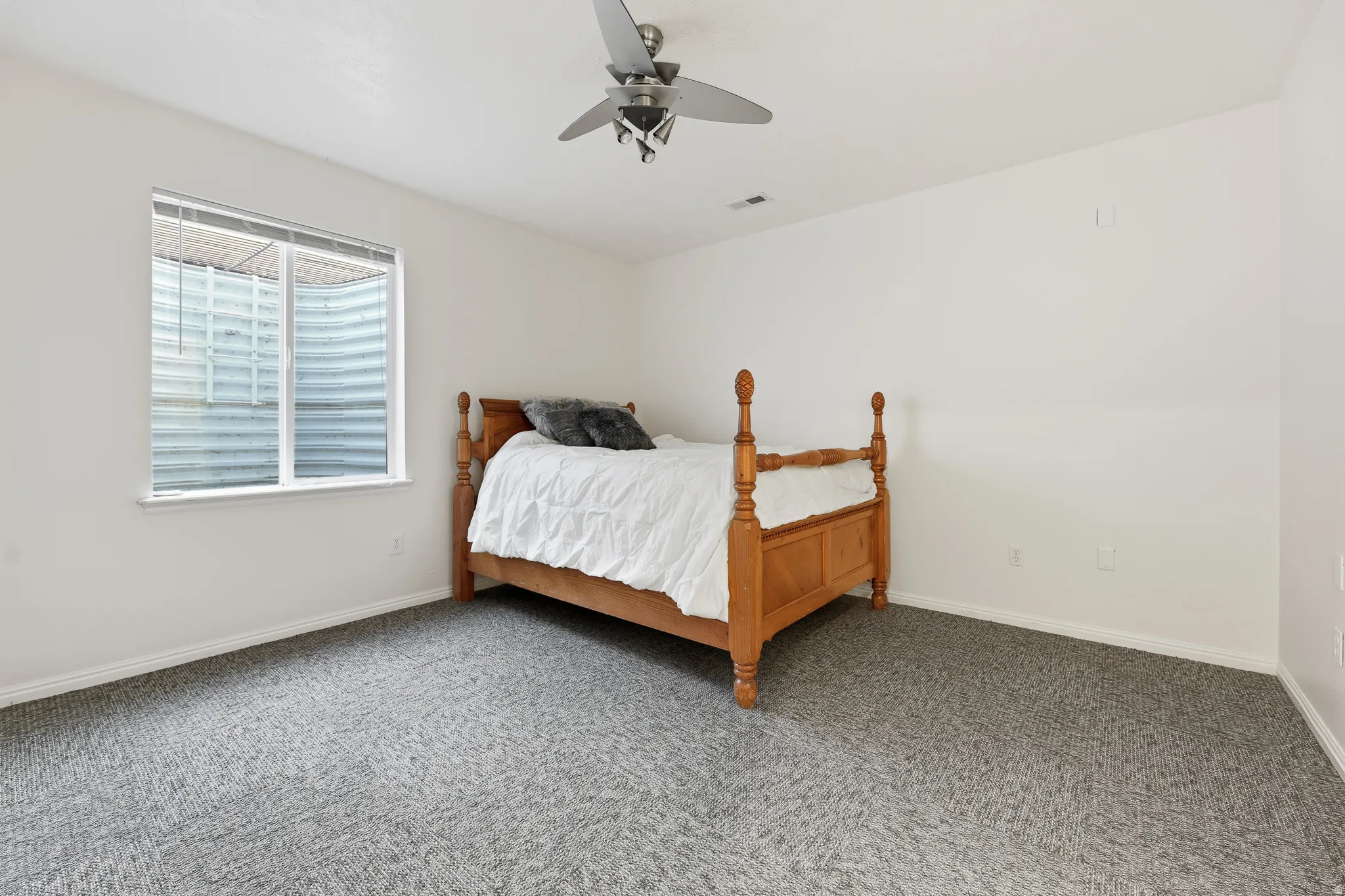 Spacious room featuring neutral carpeting, white walls, a single window, and a ceiling fan with integrated lighting