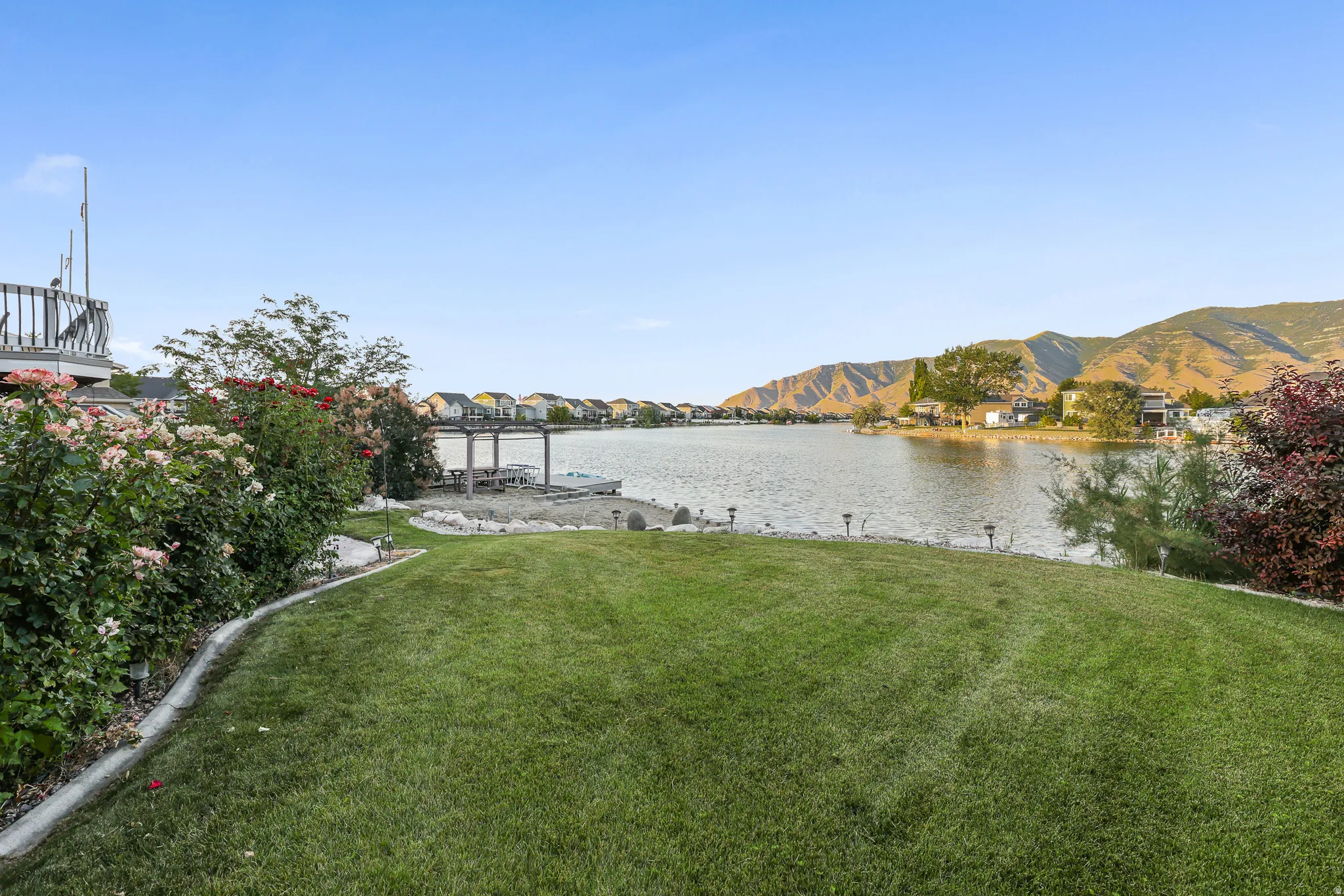 Expansive lakeside lawn with a seawall, mature flowering shrubs, and a partial upper-level deck with wooden railing