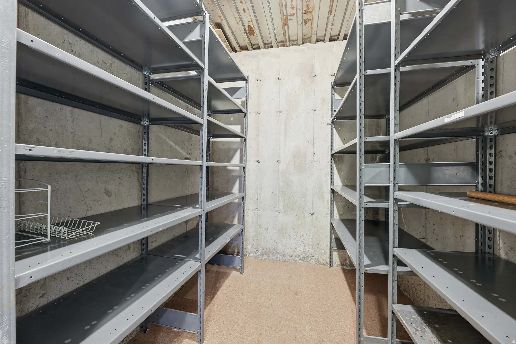 Utility room featuring extensive built-in metal shelving, exposed concrete walls, and a finished floor