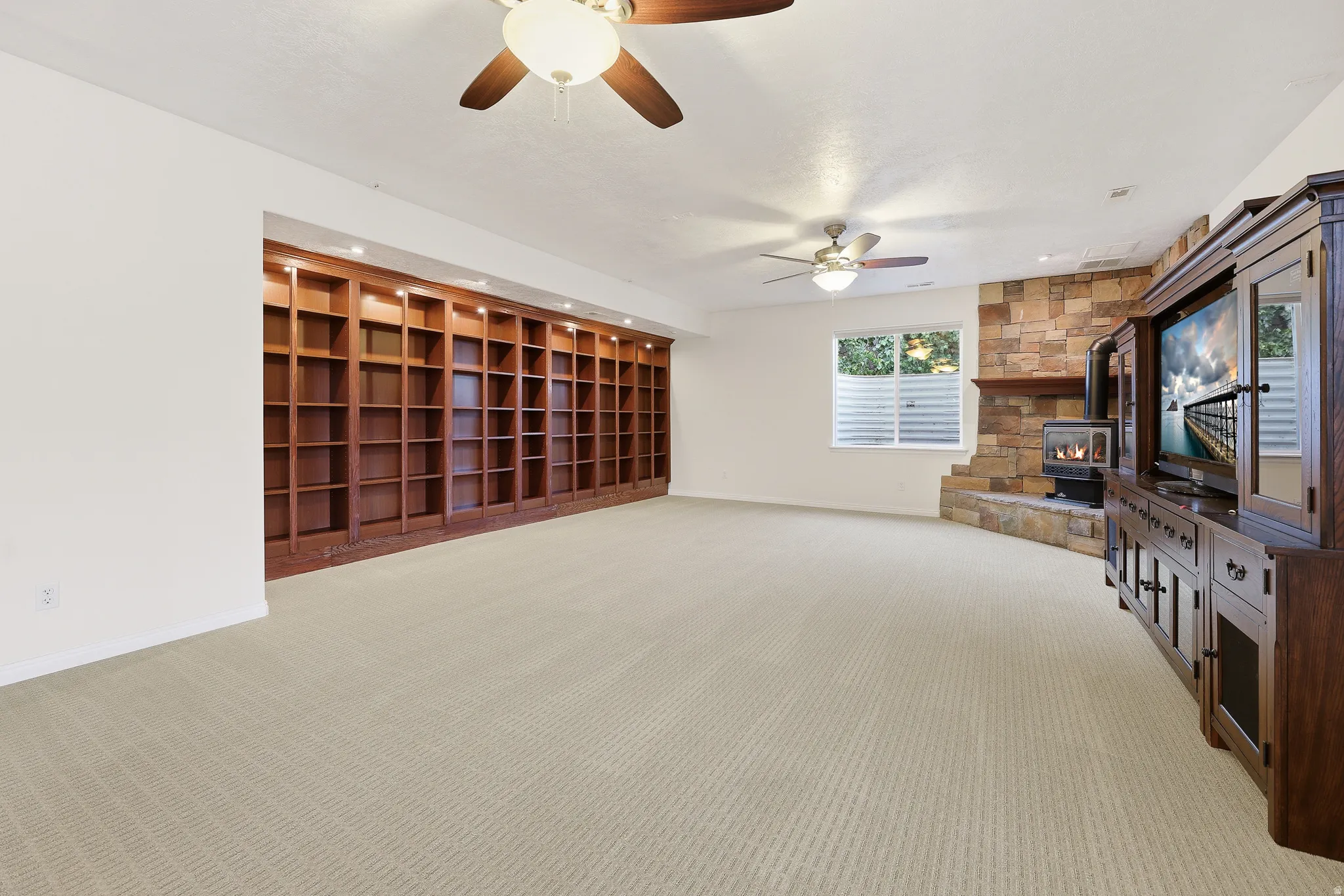 Spacious room featuring extensive built-in wooden shelving with recessed lighting, a stone-accented wall with a fireplace, and two ceiling fans