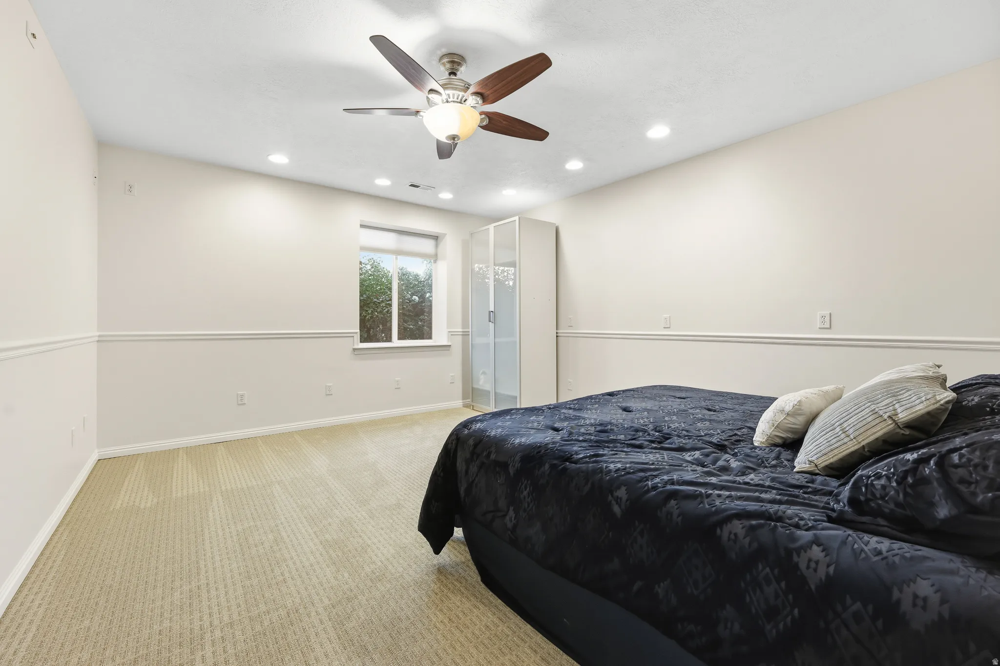 Spacious bedroom featuring neutral carpeting, chair rail molding, a ceiling fan with integrated lighting, and recessed ceiling lights