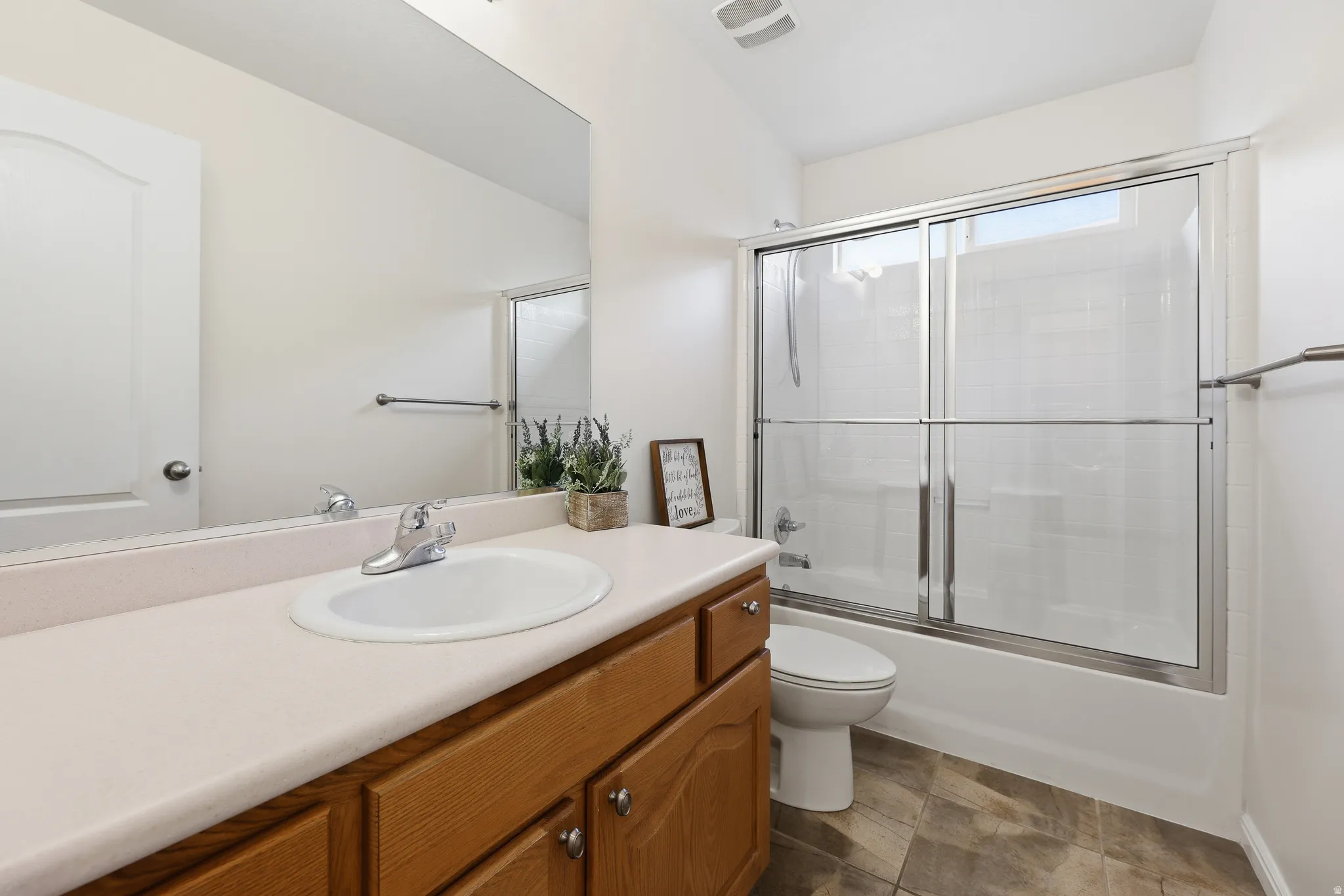 Hall Bathroom featuring a wood-finish vanity with a light-toned countertop, an integrated sink, and a framed mirror