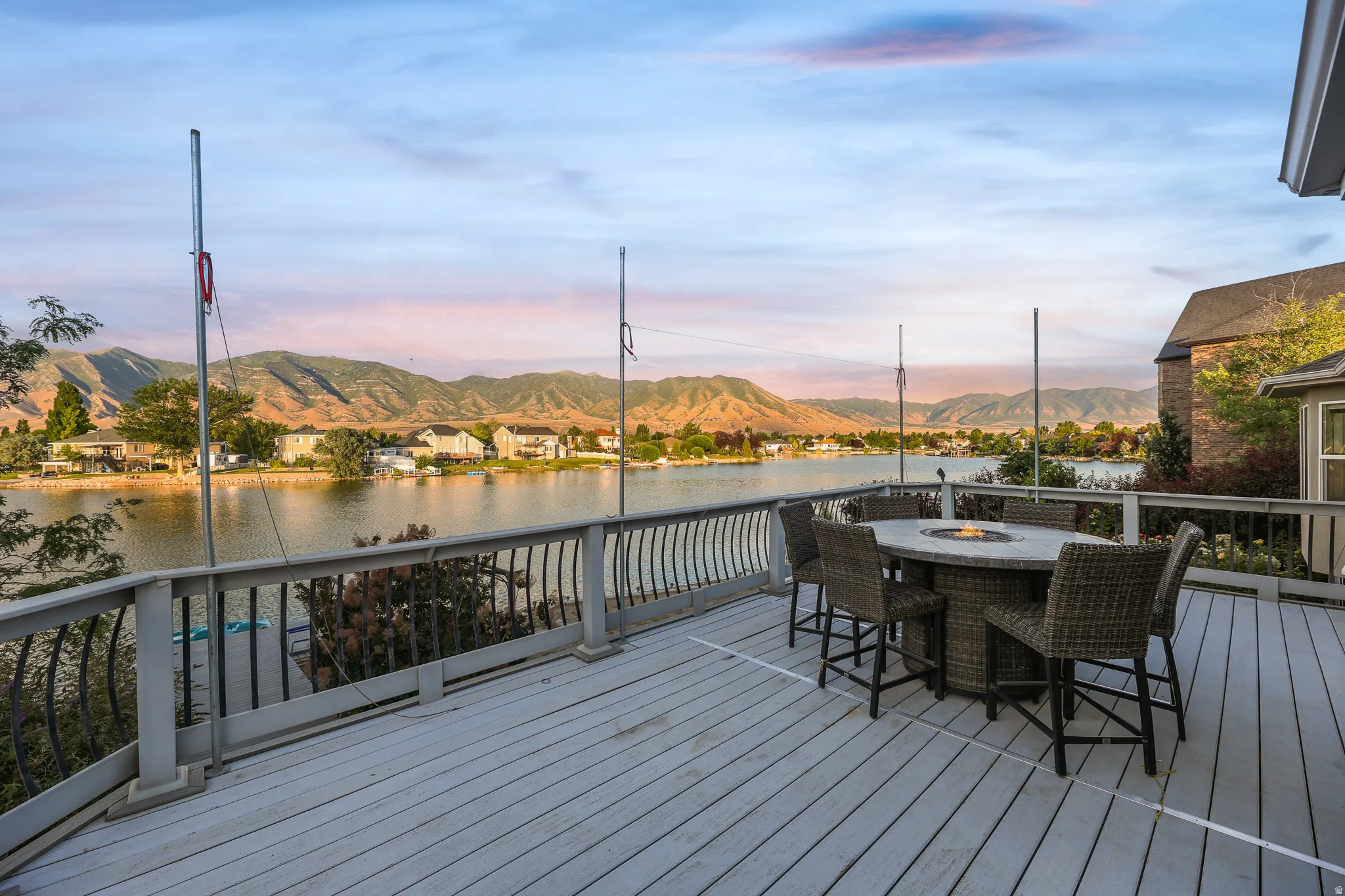 Spacious outdoor deck with wood-finish flooring and black metal railings, overlooking a body of water with distant mountains