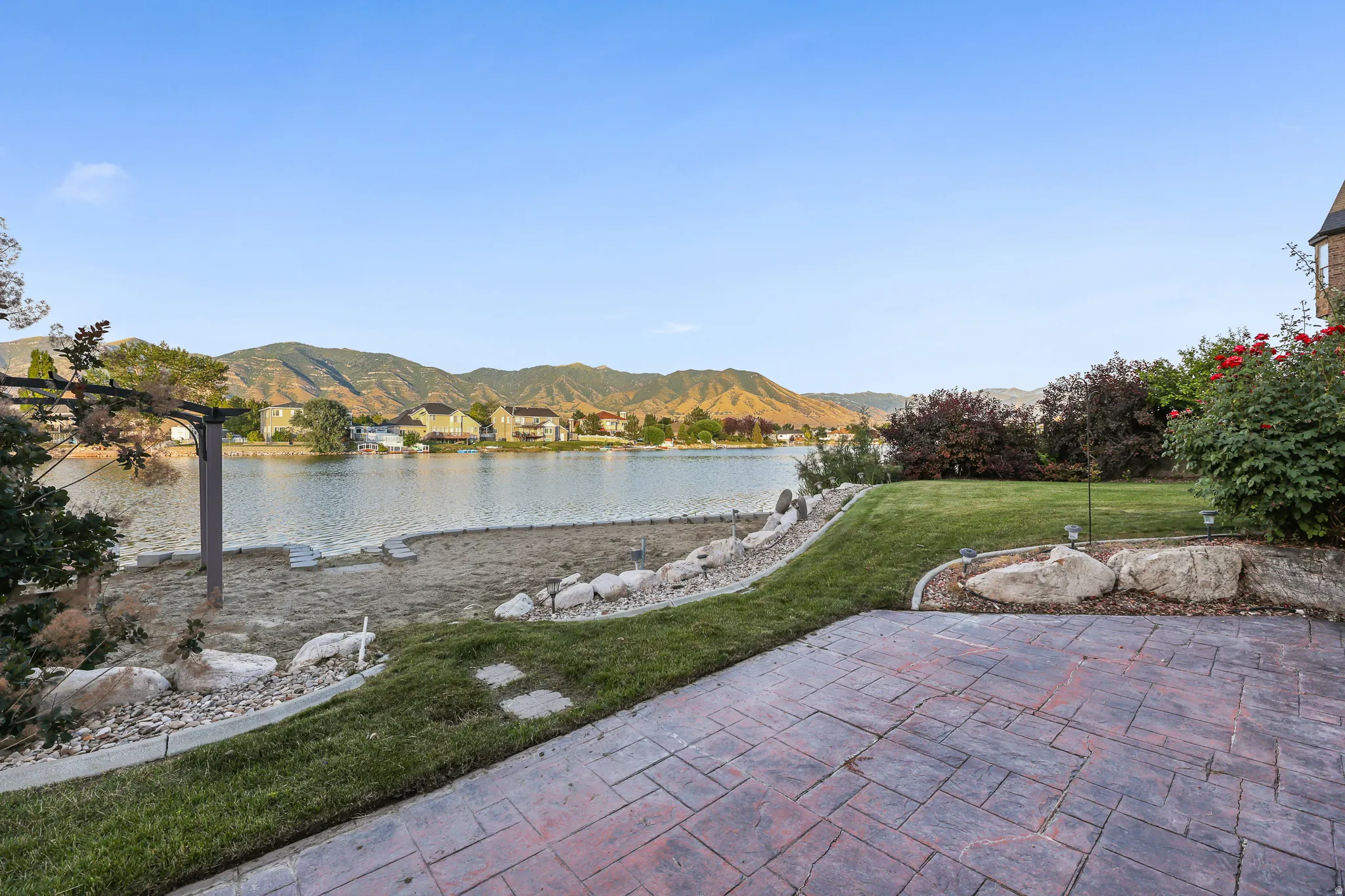 Stamped concrete patio, expansive lawn, and natural rock landscaping with sandy beach area