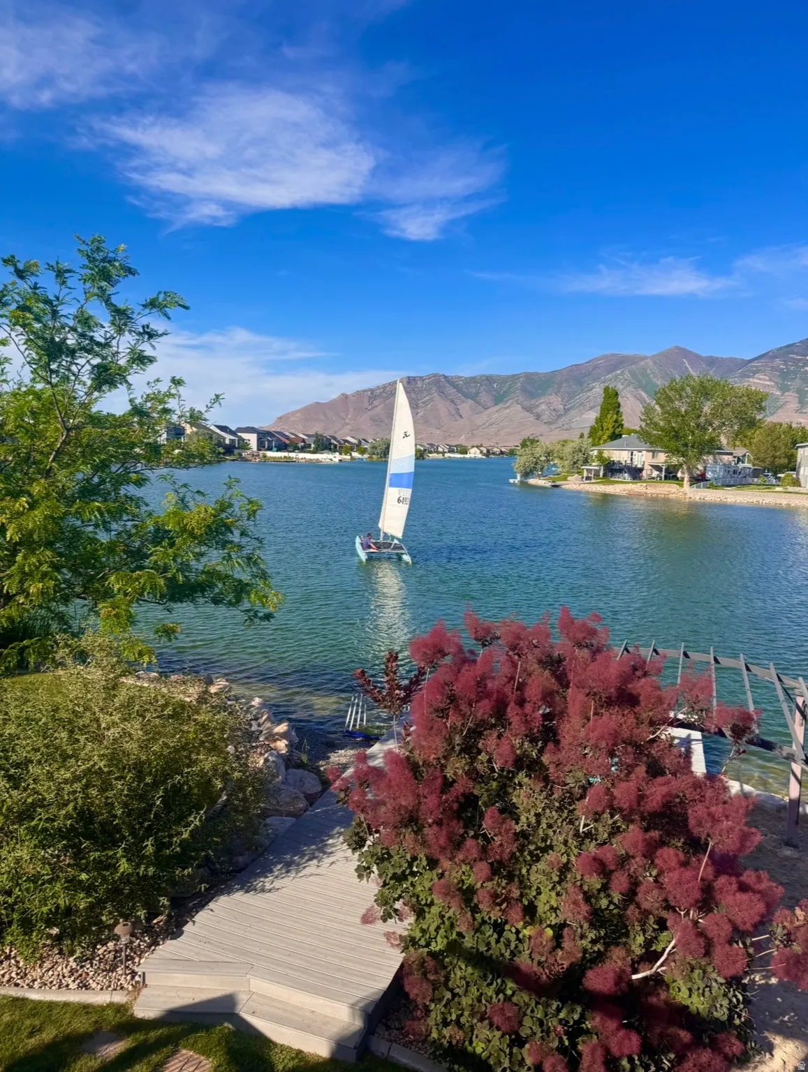 Waterfront property featuring a tiered deck, mature landscaping, and mountain backdrop. water recreation activities available