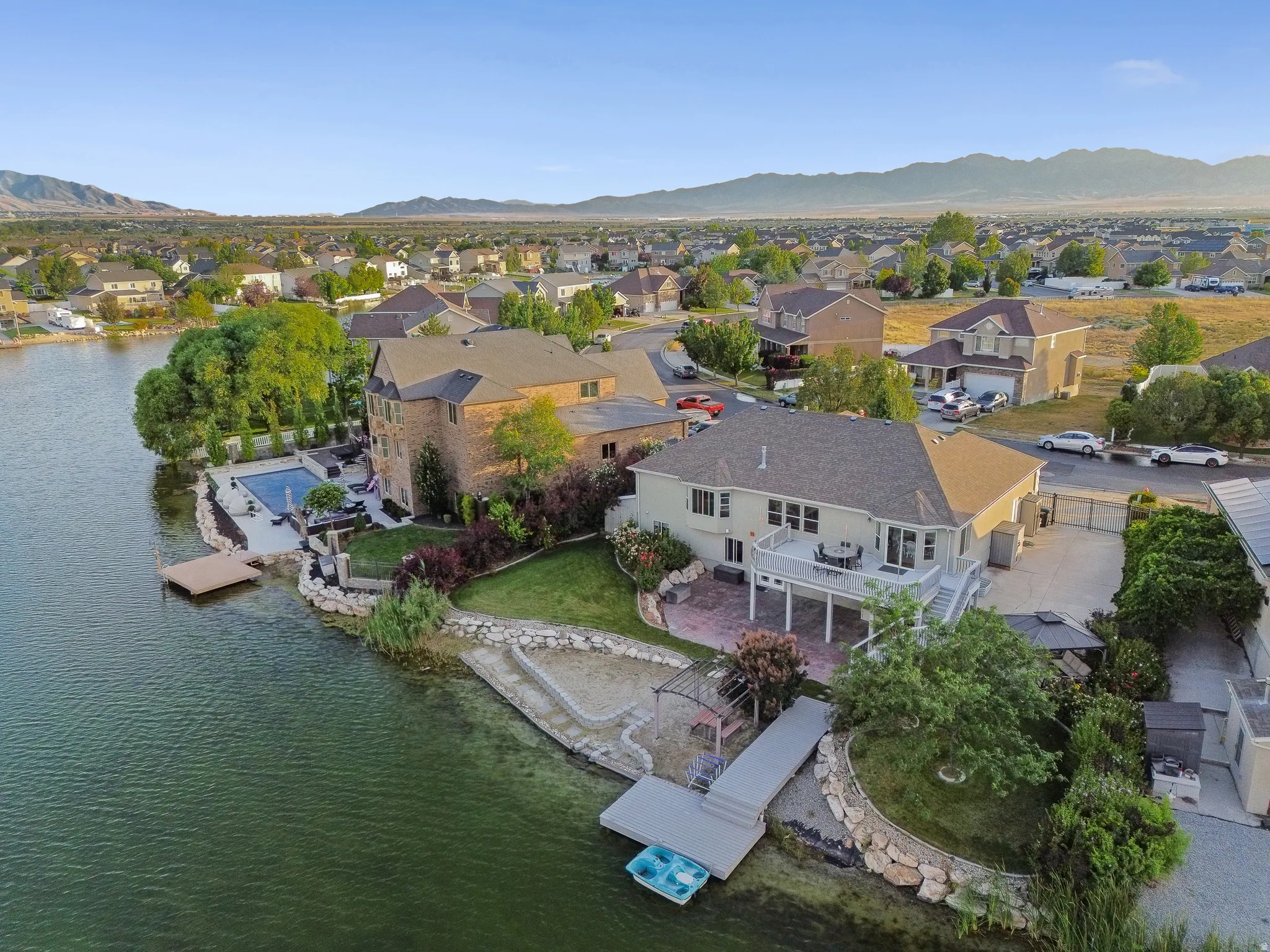 Lakefront property featuring a private boat dock, terraced backyard landscaping, an upper-level deck, a lower-level patio, and surrounding mountain scenery