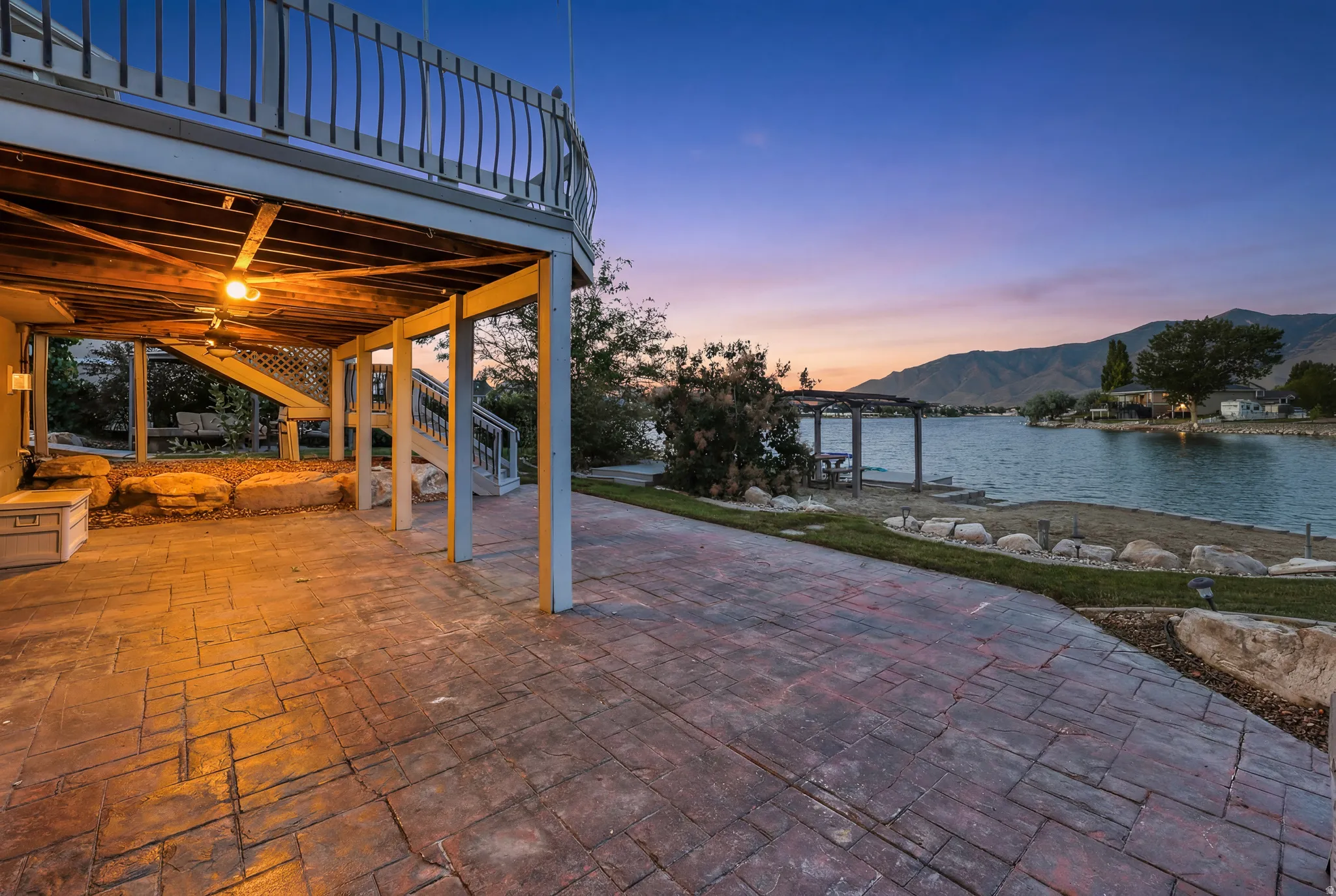 Expansive stamped concrete patio under a raised deck, featuring built-in lighting and a stone retaining wall