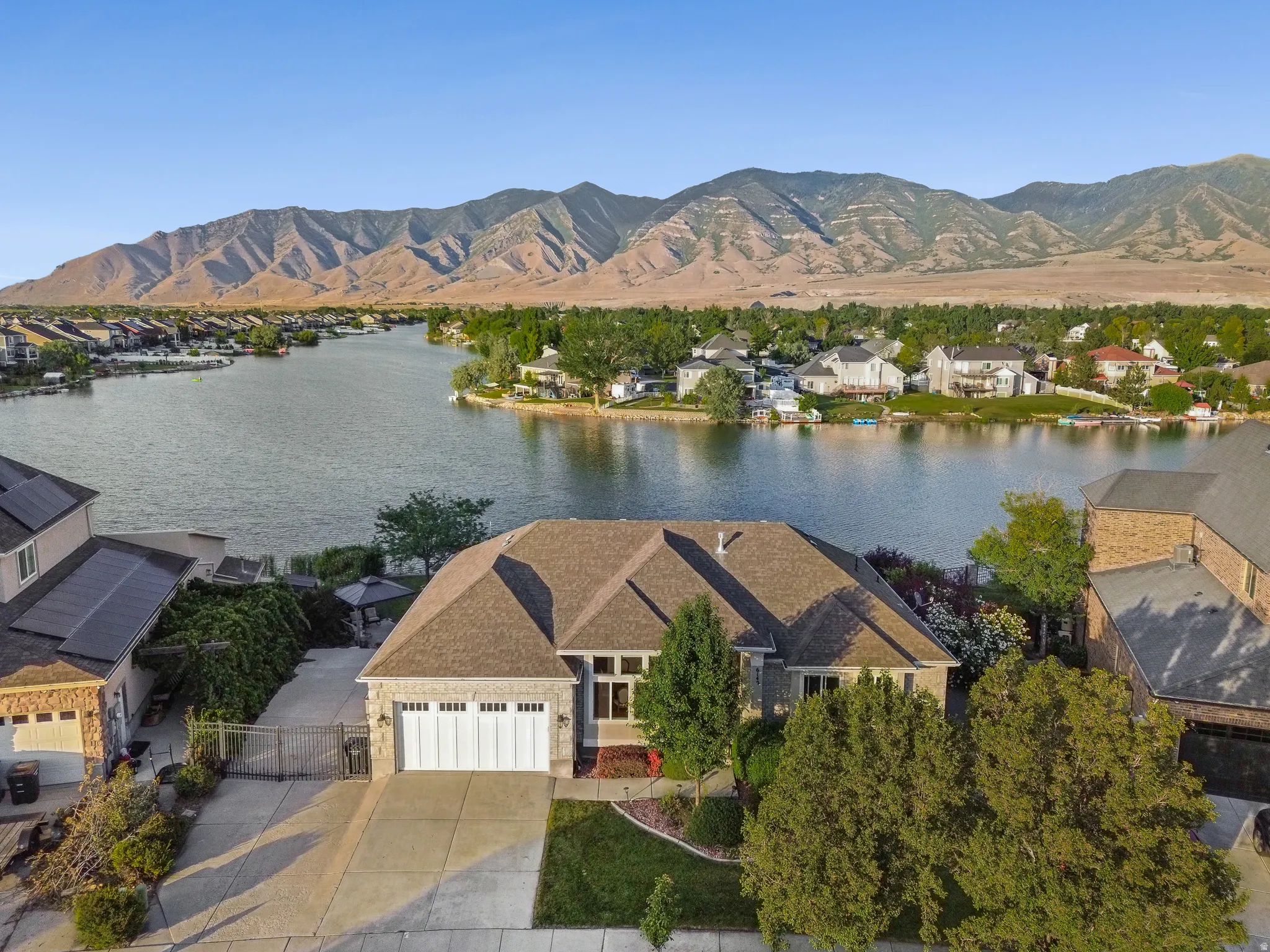 Lakefront residence featuring a two-car garage, mature landscaping, and a brown shingle roof