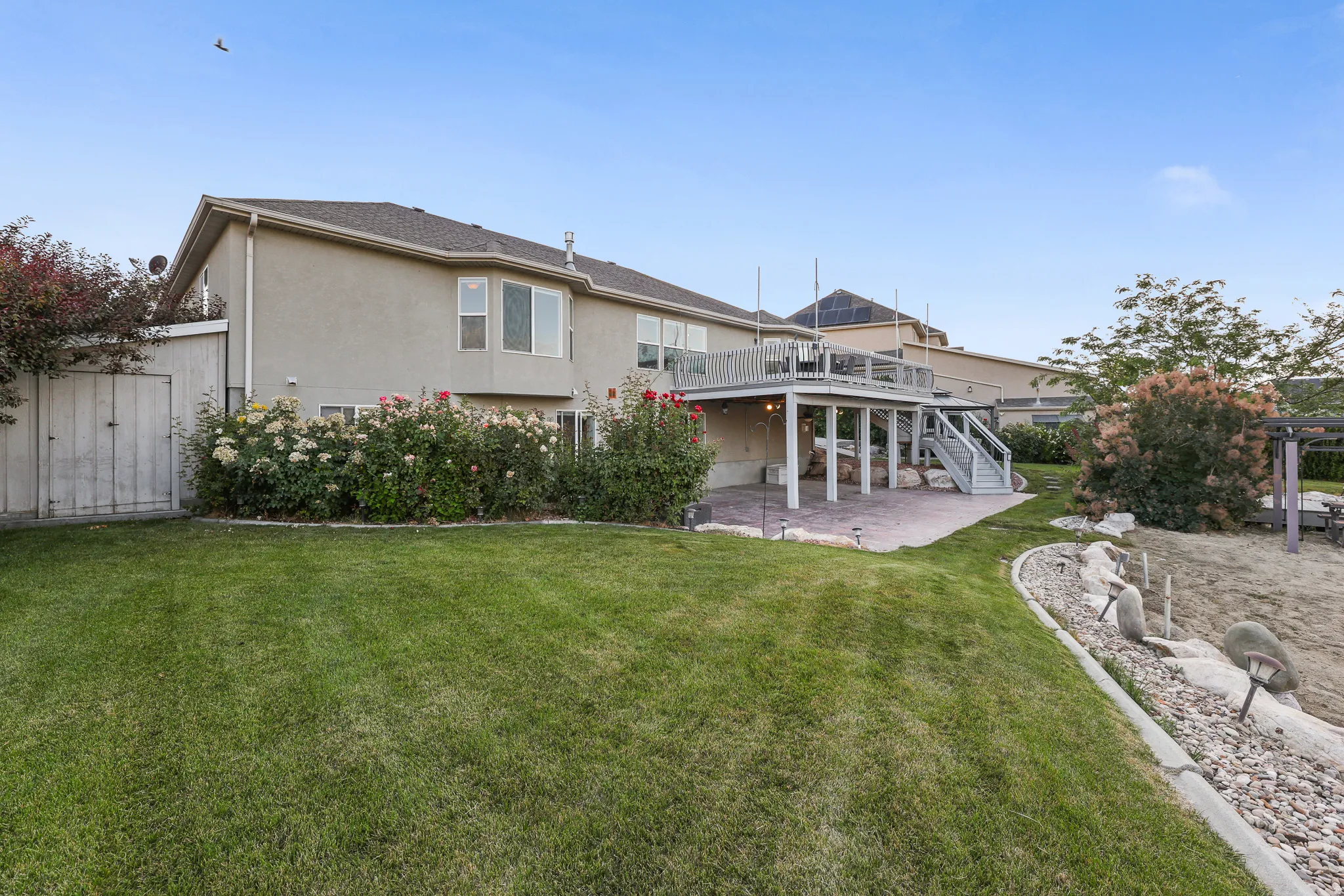 Spacious backyard featuring a multi-level deck, lower covered patio, mature landscaping, and a manicured lawn and rose garden