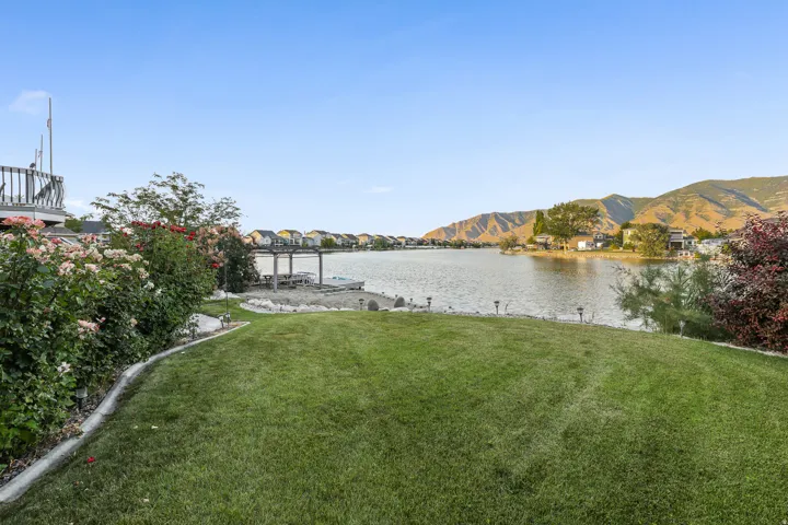 Expansive lakeside lawn with a seawall, mature flowering shrubs, and a partial upper-level deck with wooden railing