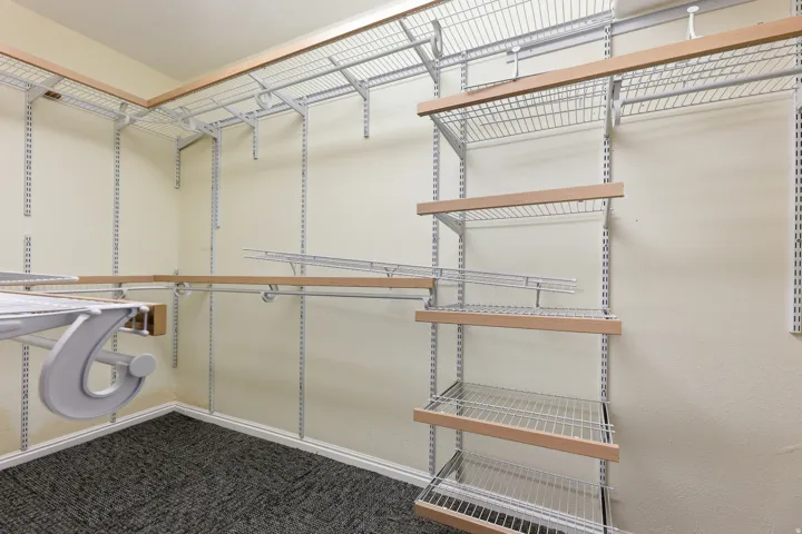 Walk-in closet featuring wire shelving, wood-finish accents, and textured carpet flooring