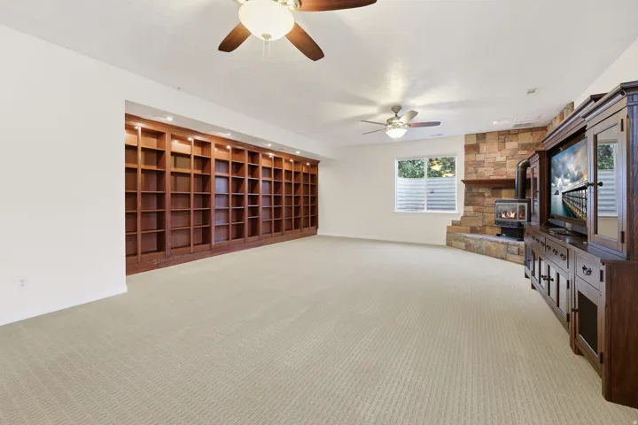 Spacious room featuring extensive built-in wooden shelving with recessed lighting, a stone-accented wall with a fireplace, and two ceiling fans