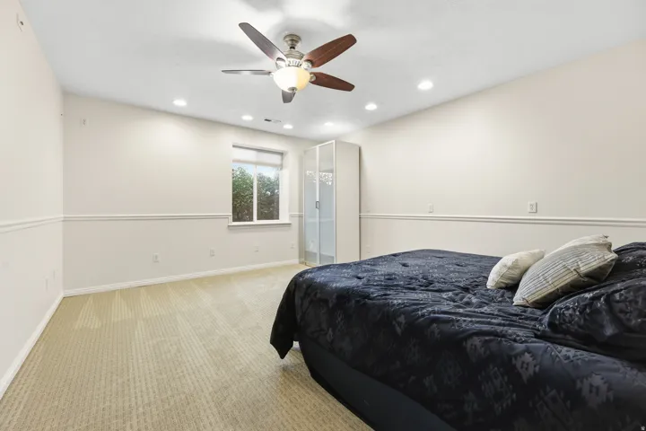 Spacious bedroom featuring neutral carpeting, chair rail molding, a ceiling fan with integrated lighting, and recessed ceiling lights