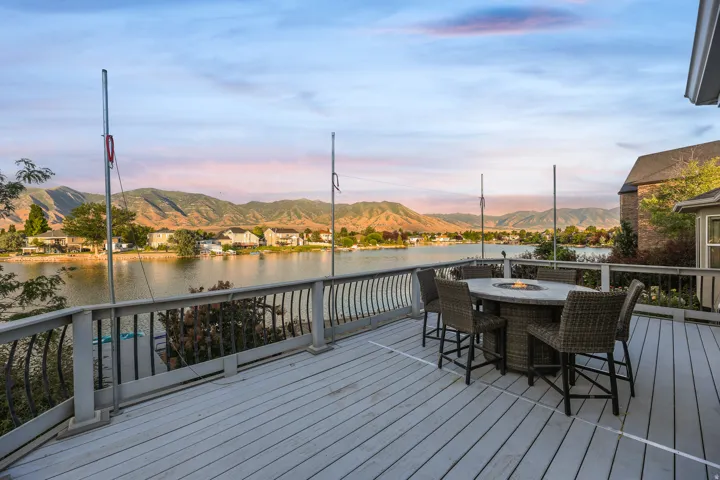 Spacious outdoor deck with wood-finish flooring and black metal railings, overlooking a body of water with distant mountains