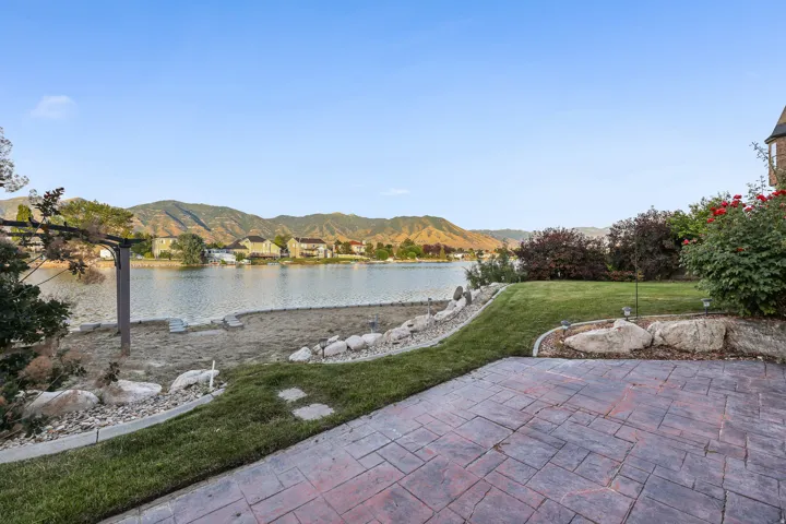 Stamped concrete patio, expansive lawn, and natural rock landscaping with sandy beach area