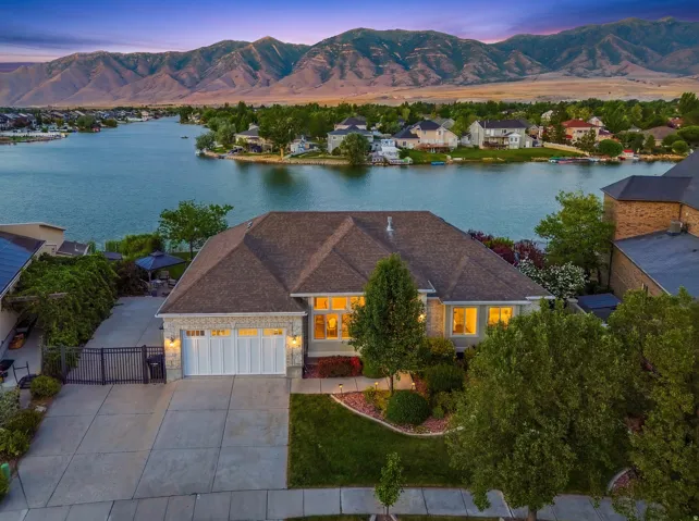 Waterfront property featuring a stone and stucco exterior, multi-pane windows, a three-car garage, and a gated driveway