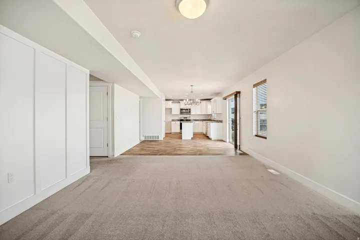 Open-concept living space featuring light-colored carpeting, white walls, and a modern ceiling light fixture