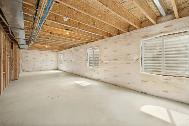 Unfinished basement featuring exposed wood joists and subfloor, concrete flooring, three egress windows with white frames, and framed wall studs