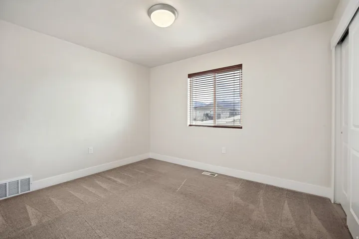 Carpeted room featuring a single window with brown blinds, a flush-mount ceiling light fixture, white baseboards, and a sliding door closet with white panels