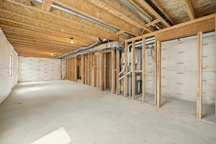 Unfinished basement featuring exposed wood joists and subflooring, concrete slab flooring, framed interior walls, and visible utility lines