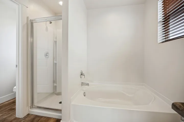 White soaking tub with chrome fixtures, a clear glass shower enclosure, and wood-finish flooring