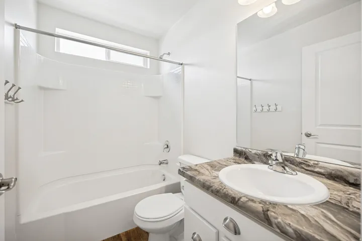 Bathroom featuring a shower-over-tub combination with a transom window, a vanity with a drop-in sink, a stone-finish countertop, and wood-finish flooring