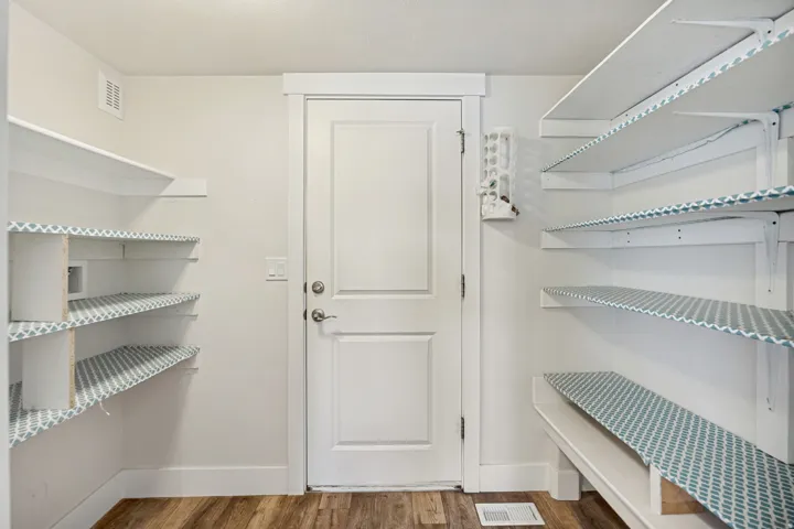 Walk-in pantry featuring extensive white shelving, wood-finish flooring, and a solid white door