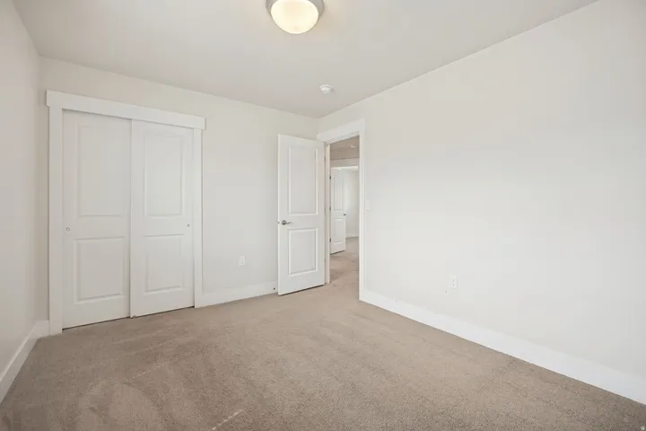 Carpeted room with a flush-mount ceiling light fixture, featuring a sliding double-panel closet door with white trim, and a matching interior door with silver hardware