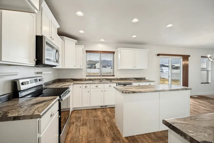 Bright kitchen featuring white cabinetry, dark stone-finish countertops, stainless steel appliances, a central island, and wood-finish flooring