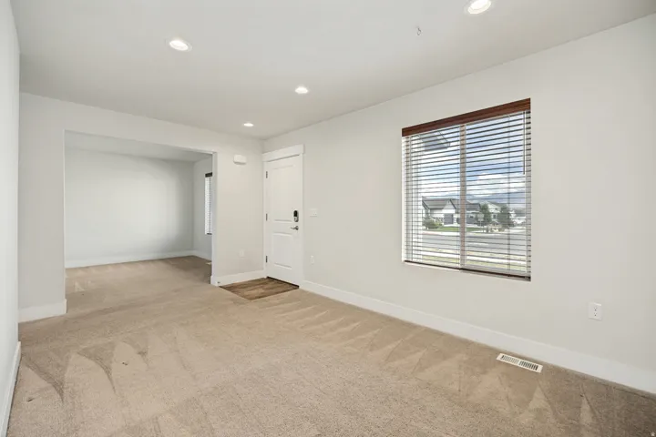 Spacious living area featuring neutral carpeting, recessed lighting, white trim, and a front entry door with a smart lock
