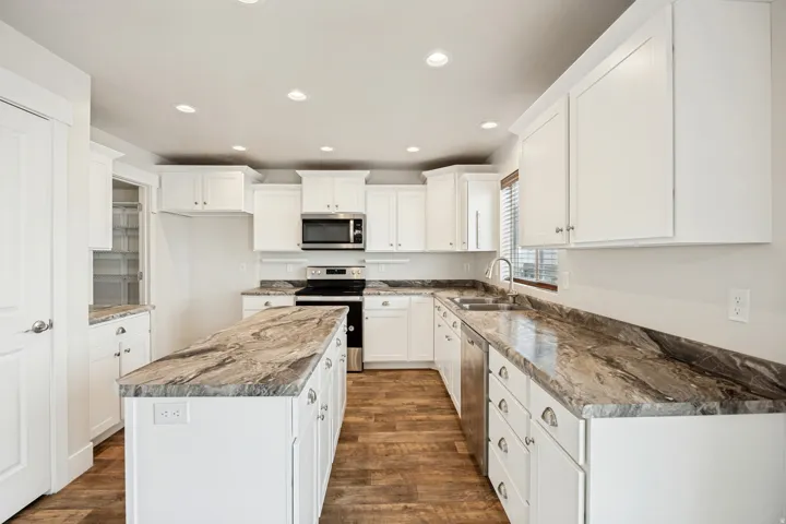 Kitchen featuring a central island, white cabinetry, integrated stainless steel appliances, wood-finish flooring, and natural stone countertops